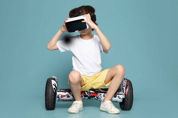 A front view child boy in white t-shirt playing vr on segway on the blue space