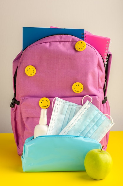 Free photo front view child school bag with copybooks spray and masks on yellow desk