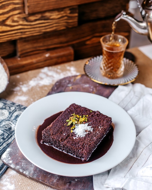 Front view choco cake tasty inside white plate along with hot tea on the brown surface