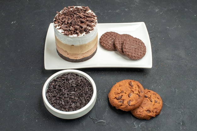 Front view chocolate cake and biscuits on white rectangular plate bowl with dark chocolate biscuits on dark isolated background