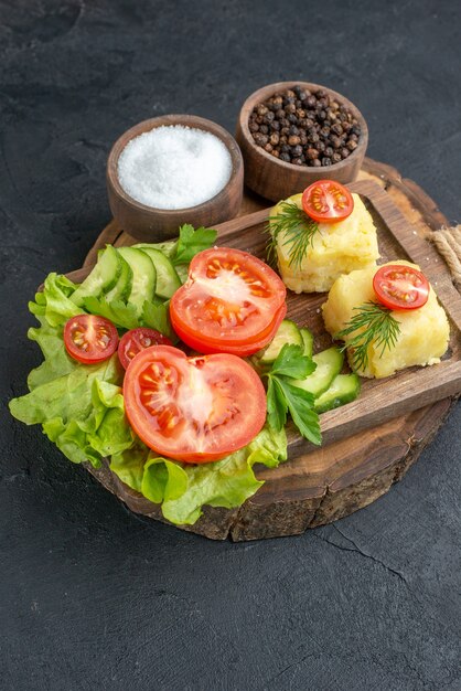 Front view of chopped and whole fresh vegetables cheese on cutting board and spices on black surface