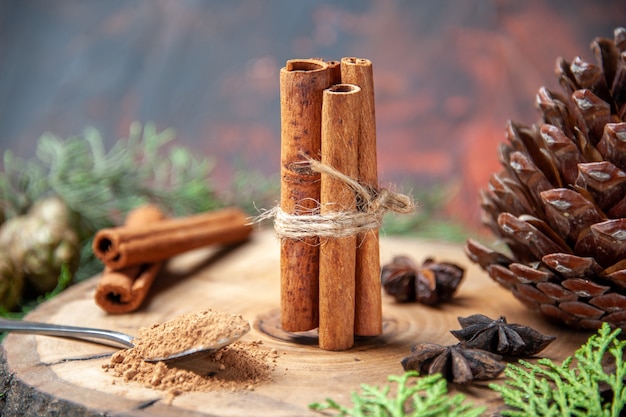 Front view cinnamon sticks cinnamon powders pinecone anises on wood board on dark