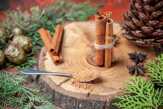 Free Photo front view cinnamon sticks cinnamon powders pinecone anises on wood board spoon with cinnamon powder on dark