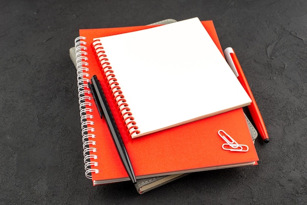 Free Photo front view of closed spiral notebooks in different sizes and pens on black