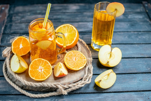 Front view cocktail cut oranges and apples on wood board on dark isolated background