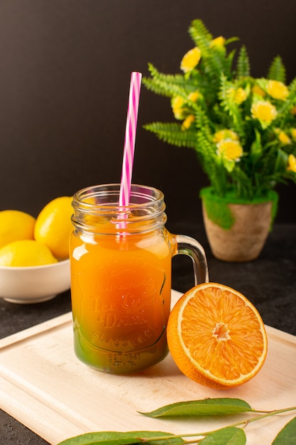 A front view cold cocktail colored inside glass cans with colorful straw lemons green leaves on the wooden cream desk and dark