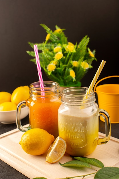 A front view cold cocktails colored inside glass cans with colorful straws lemons green leaves flowers on the wooden cream desk and dark