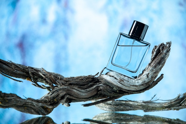 Free photo front view cologne bottle on rotten tree branch on light blue background