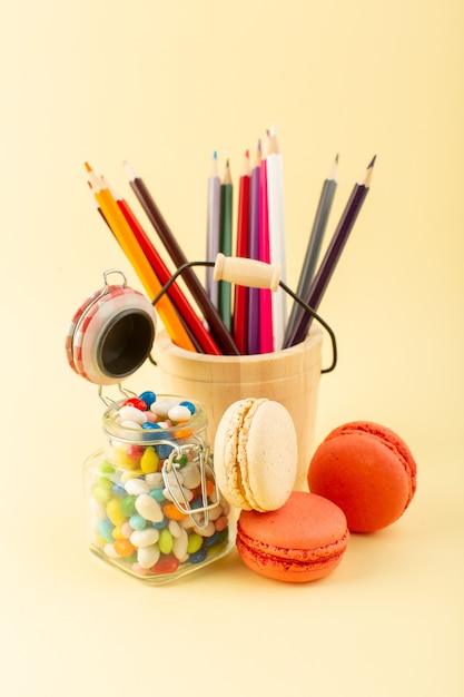 A front view colorful candies with french macarons and multicolored pencils