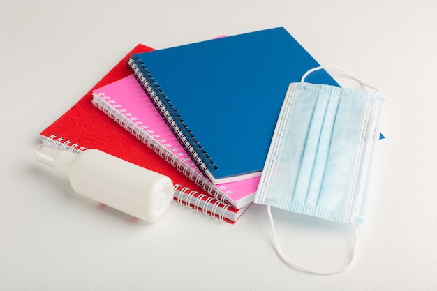 Front view colorful copybooks with spray and mask on white surface