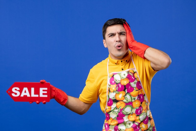 Free photo front view confused male housekeeper in yellow t-shirt holding sale sign holding his head on blue space