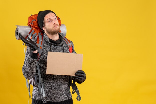 Front view of confused man camper with leather gloves and backpack holding blank cardboard