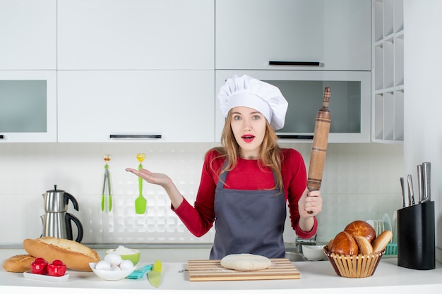 Free photo front view confused woman in cook hat and apron holding rolling pin in the kitchen