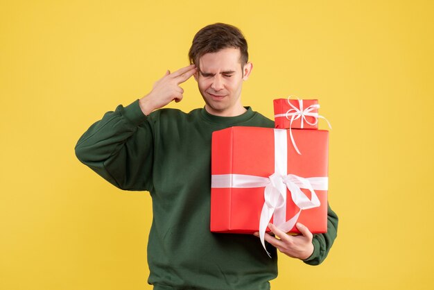 Front view confused young man with xmas gift standing on yellow 