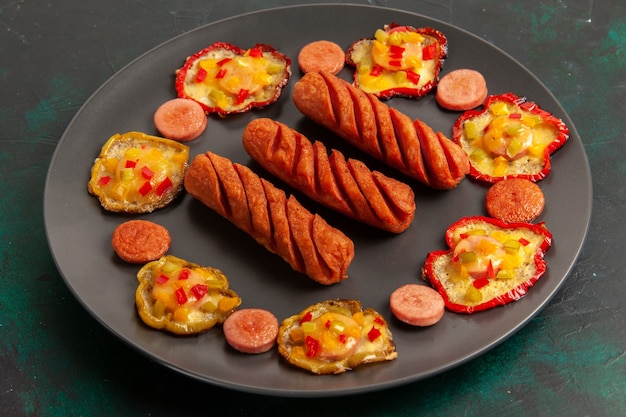 Free photo front view cooked bell-peppers with sausages inside plate on dark surface