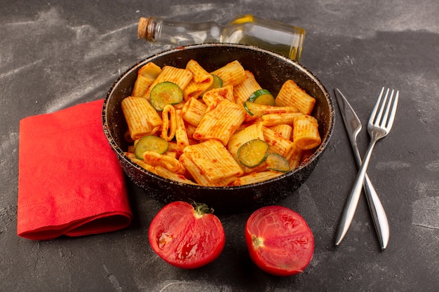 A front view cooked italian pasta with tomato sauce and cucumber inside pan on the dark surface