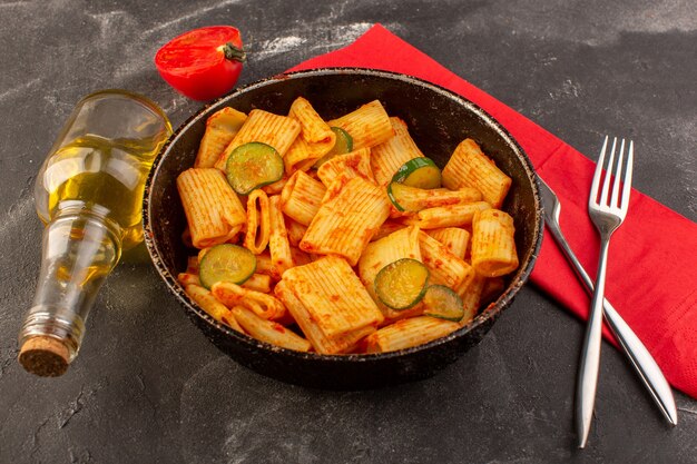 A front view cooked italian pasta with tomato sauce and cucumber inside pan on the dark surface