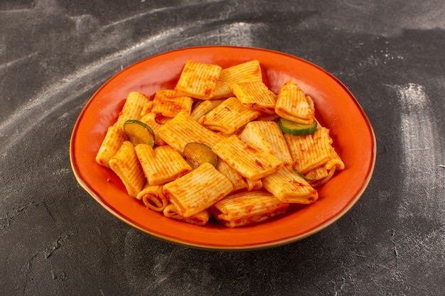 A front view cooked italian pasta with tomato sauce and cucumber inside plate on the dark surface