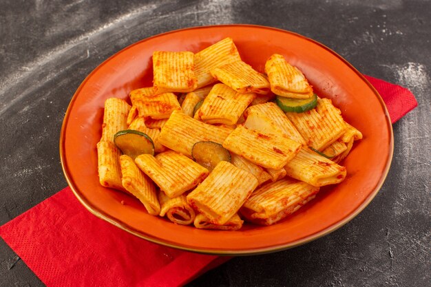 A front view cooked italian pasta with tomato sauce and cucumber inside plate on the dark surface