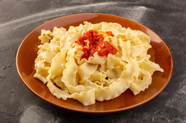 A front view cooked italian pasta with tomato sauce inside plate on the grey surface