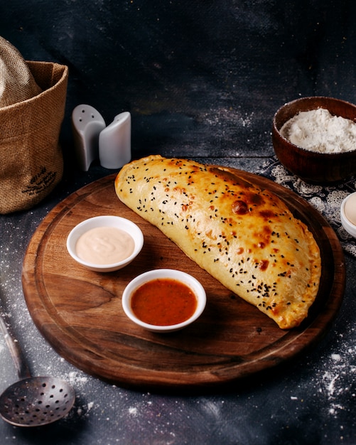 Front view cooked pastry along with red and white sauces on the brown wooden round desk and grey floor