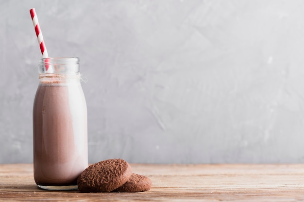 Front view cookies and chocolate milk in bottle with straw on table