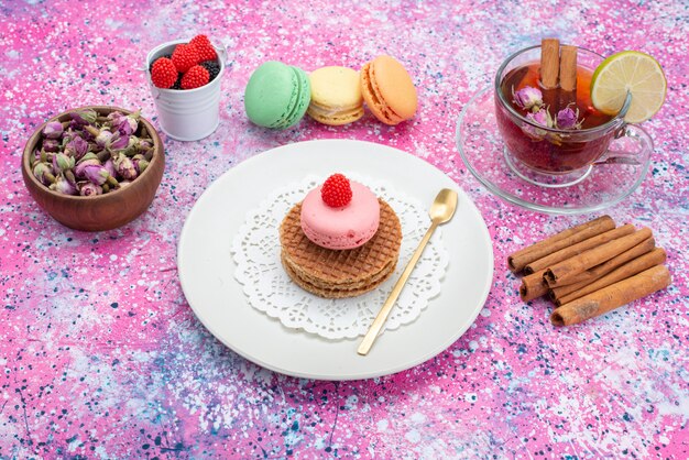 Front view of cookies and macarons with cinnamon tea on the colored surface