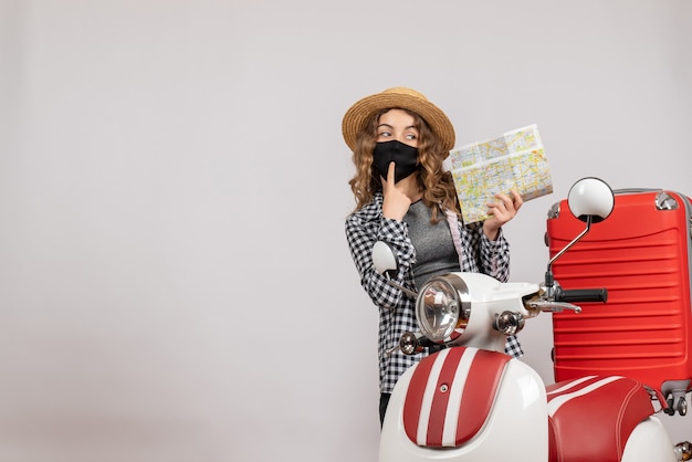 Front view of cool young girl with black mask holding map standing near red moped