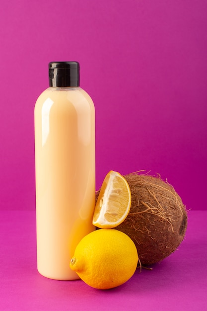 A front view cream colored bottle plastic shampoo can with black cap along with lemons and coconut isolated on the purple background cosmetics beauty hair