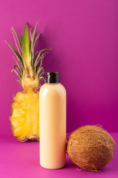 A front view cream colored bottle plastic shampoo can with black cap along with lemons pineapple and coconut isolated on the purple background cosmetics beauty fruits