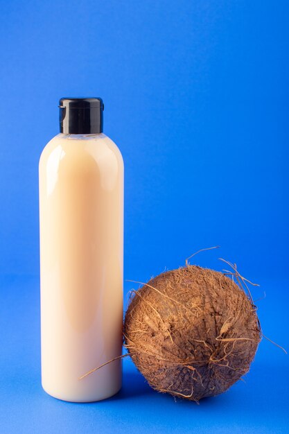 A front view cream colored bottle plastic shampoo can with black cap isolated along with coconut on the blue background cosmetics beauty hair