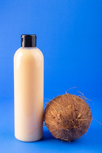 A front view cream colored bottle plastic shampoo can with black cap isolated along with coconut on the blue background cosmetics beauty hair