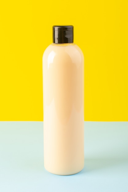 A front view cream colored bottle plastic shampoo can with black cap isolated yellow-iced-blue background cosmetics beauty hair