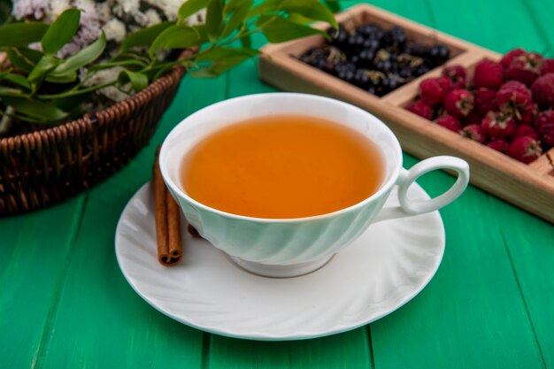 Front view of cup of tea with cinnamon raspberries and black currants on a green surface