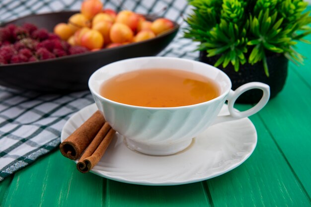 Front view of cup of tea with cinnamon raspberries and white cherries on a green surface