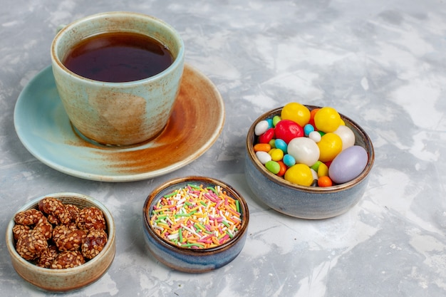 Front view cup of tea with colorful candies on light-white desk