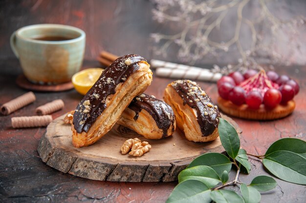 Front view cup of tea with delicious choco eclairs on a dark background