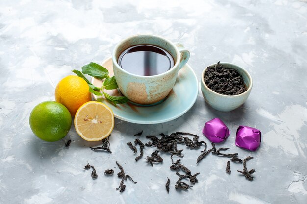 Front view cup of tea with fresh lemons candies and dried tea on the white table, tea fruit citrus color