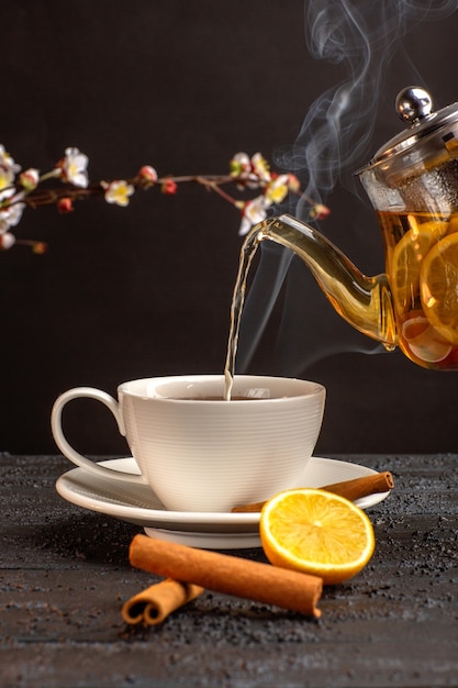 Front view cup of tea with lemon cinnamon and kettle on grey desk