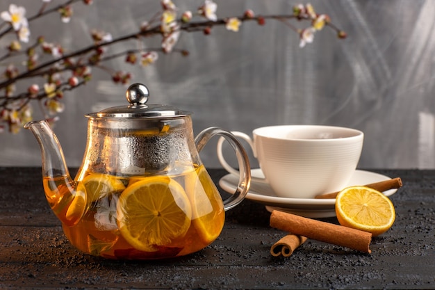 Front view cup of tea with lemon cinnamon and kettle on grey surface