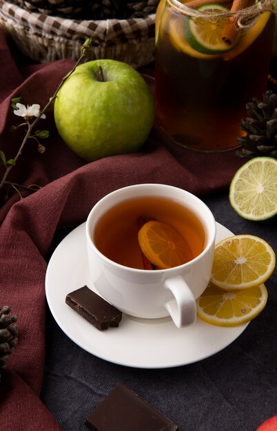 Front view cup of tea with lemon slices and dark chocolate with a green apple on the table