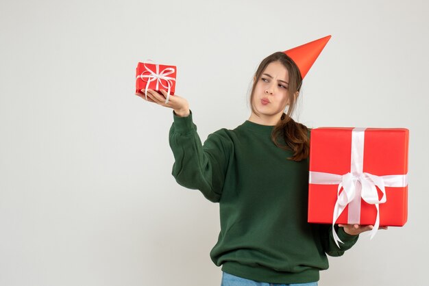 Front view curious girl with party cap comparing her xmas gifts