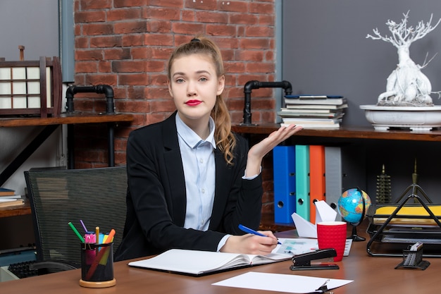 Free photo front view of curious young female sitting at a table and writing on document in the office