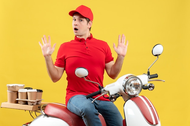 Front view of curious young guy wearing red blouse and hat delivering orders on yellow background