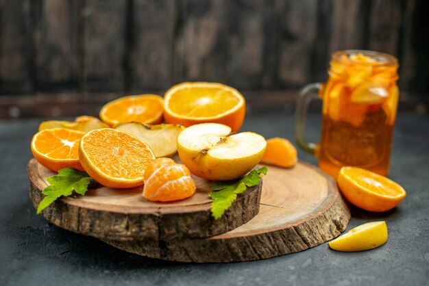 Front view cut apples and oranges on wood board cocktail on dark background