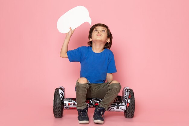 A front view cute boy in blue t-shirt sitting on the segway on the pink space