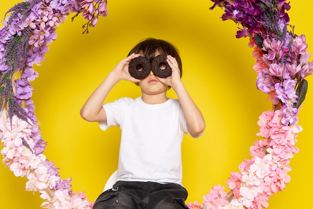 Free photo a front view cute boy with choco donuts in white t-shirt on the yellow space