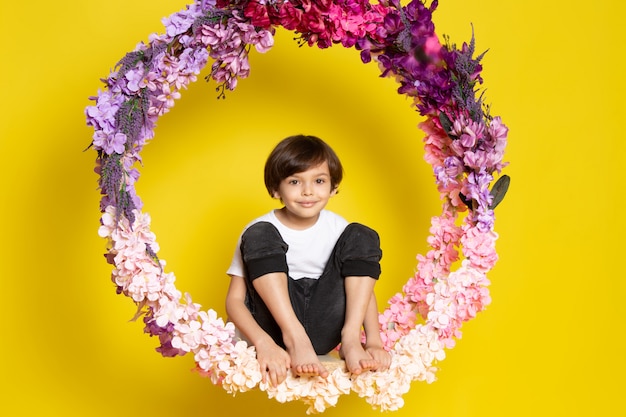 Free photo a front view cute kid in white t-shirt sitting on the flower made stand on the yellow desk