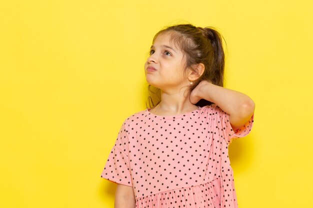 A front view cute little kid in pink dress posing with displeased expression