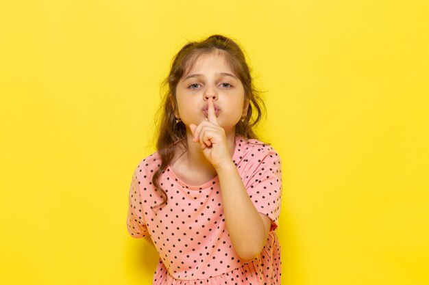 A front view cute little kid in pink dress showing silence sign